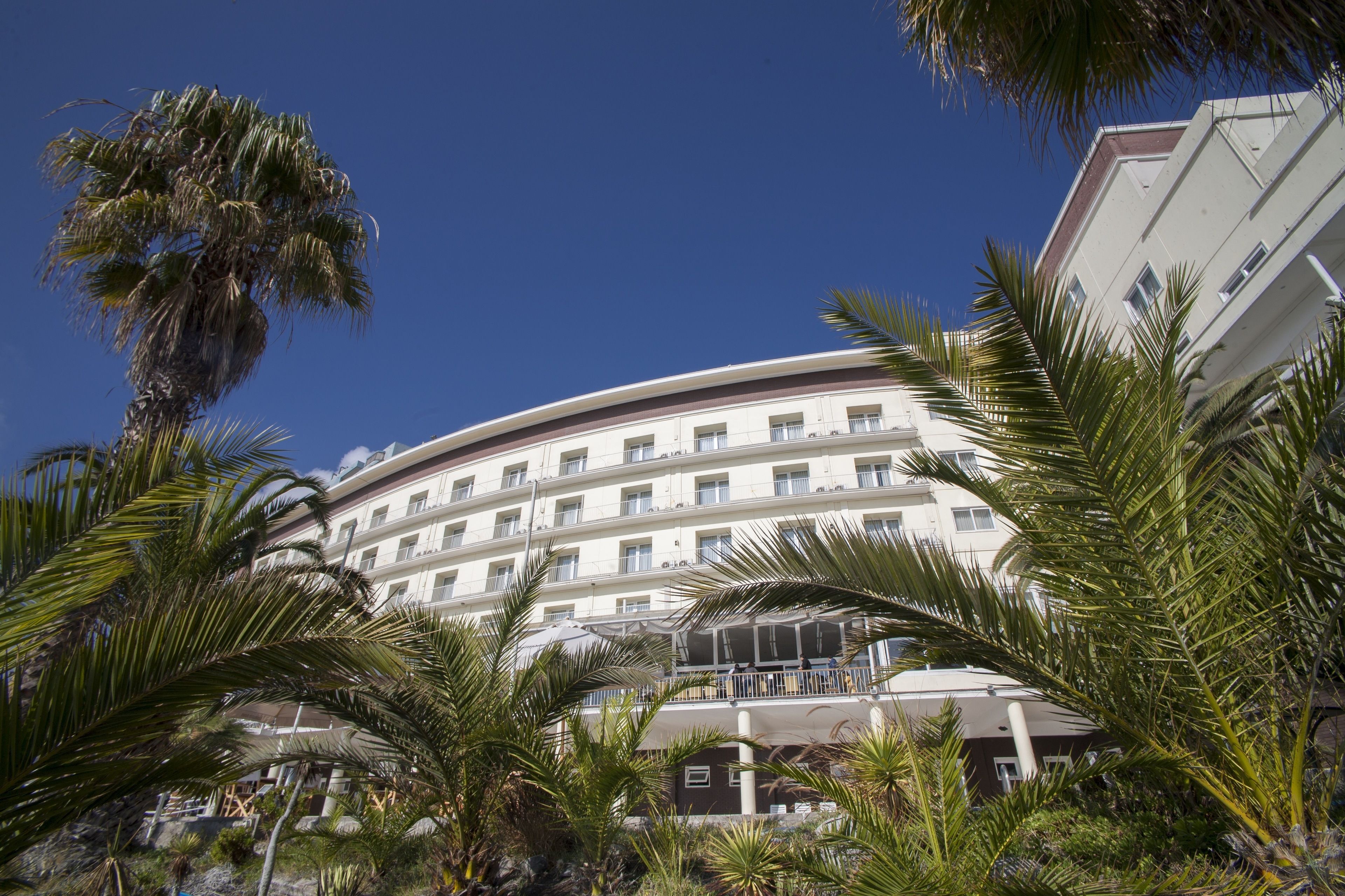 Een hotel met meerdere verdiepingen en balkons, omringd door palmbomen.