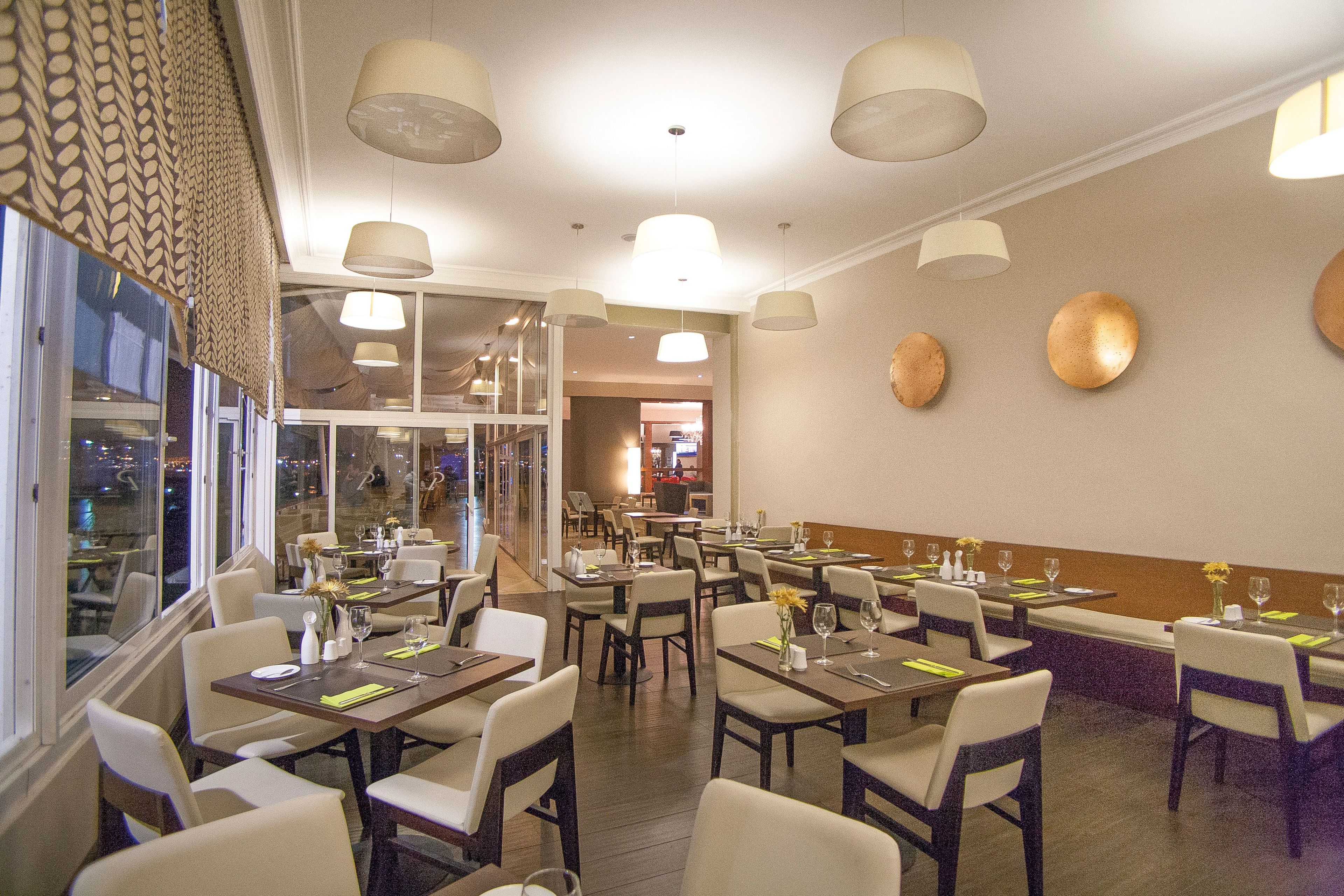A dining area with tables set for service, large windows, and a view of the city at night.