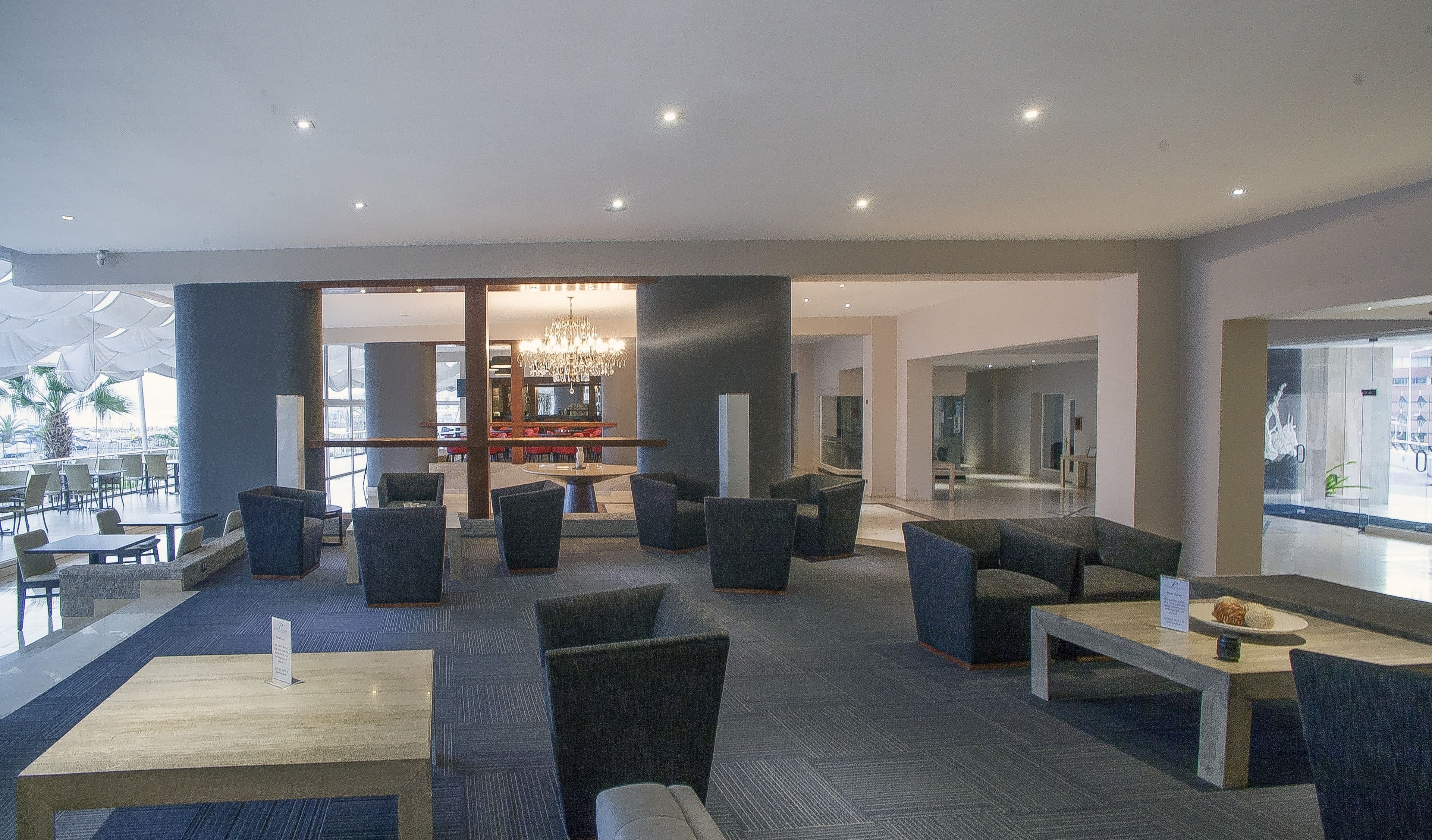 A modern lounge area with seating and a bar, large windows, and a view of the outdoors.