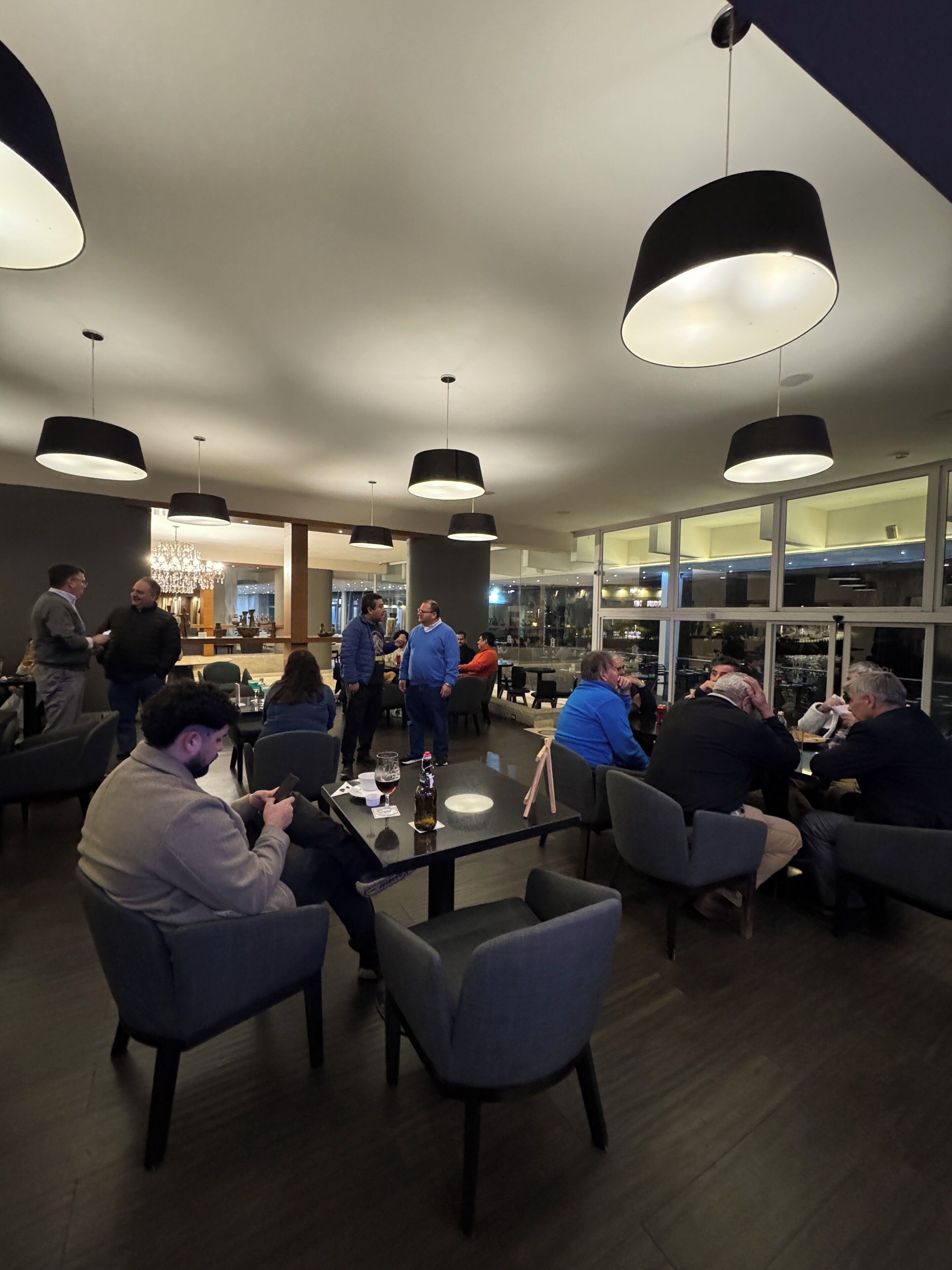 A modern restaurant interior with round tables, black pendant lighting, and a view of the city through large windows.