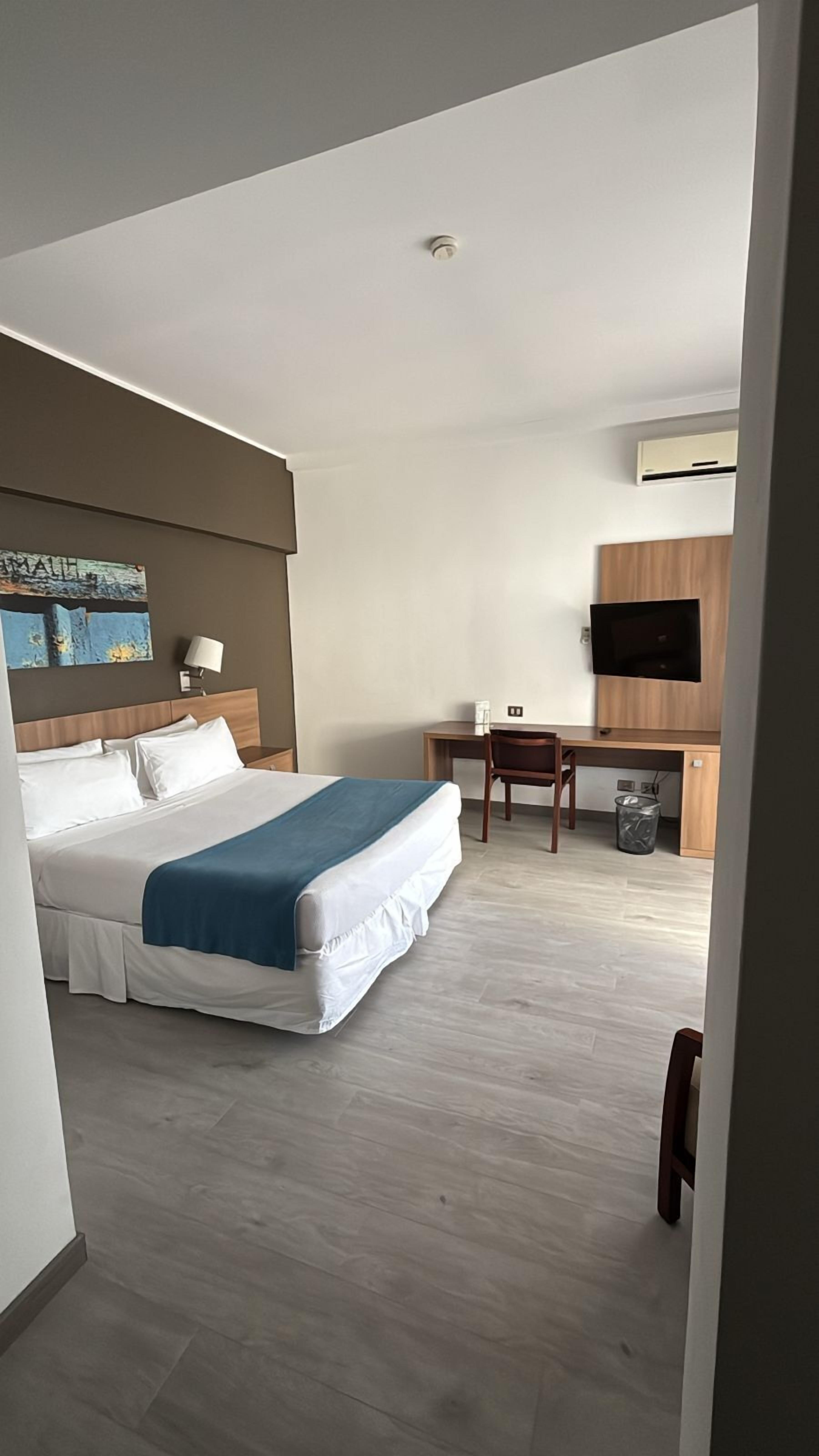 Een hotelkamer met een bed, bureau, stoel, televisie en een prullenbak.