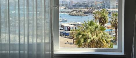 Ventana con vista a un puerto deportivo, barcos y un paisaje montañoso.