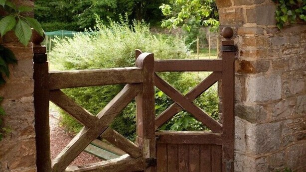 A stone archway with a wooden gate, a lantern, and a potted plant. - Hotel Lafarques (Pepinster)