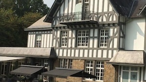 A large, two-story building with a traditional half-timbered facade, multiple windows, and a covered outdoor seating area with tables and umbrellas. - Hotel Lafarques (Pepinster)