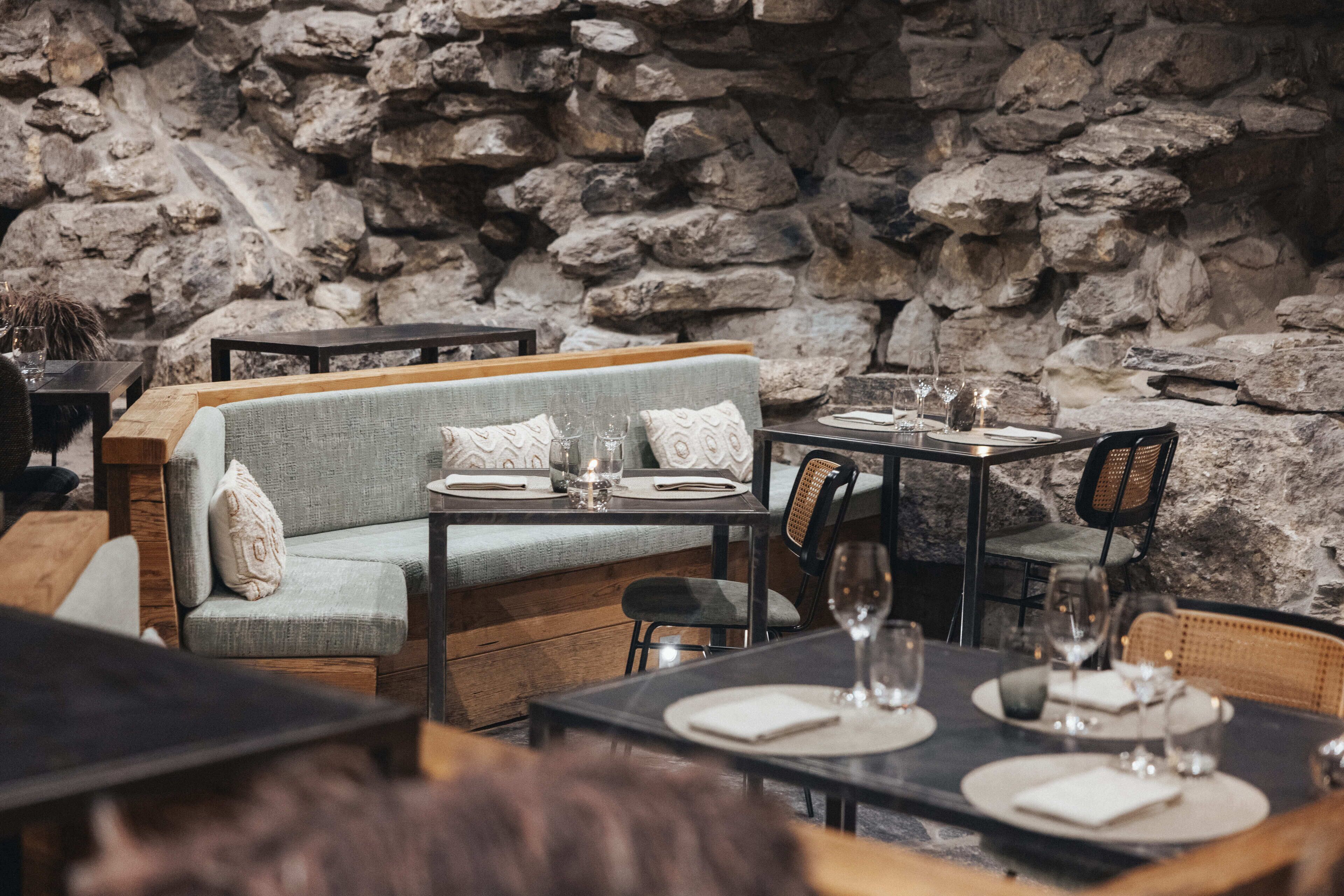 A restaurant with stone walls, a wooden bench, and tables set for dining.