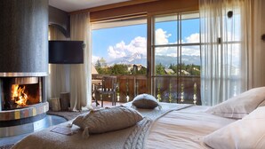 Un dormitorio con chimenea, un ventanal con vistas a la montaña y un balcón con una silla.