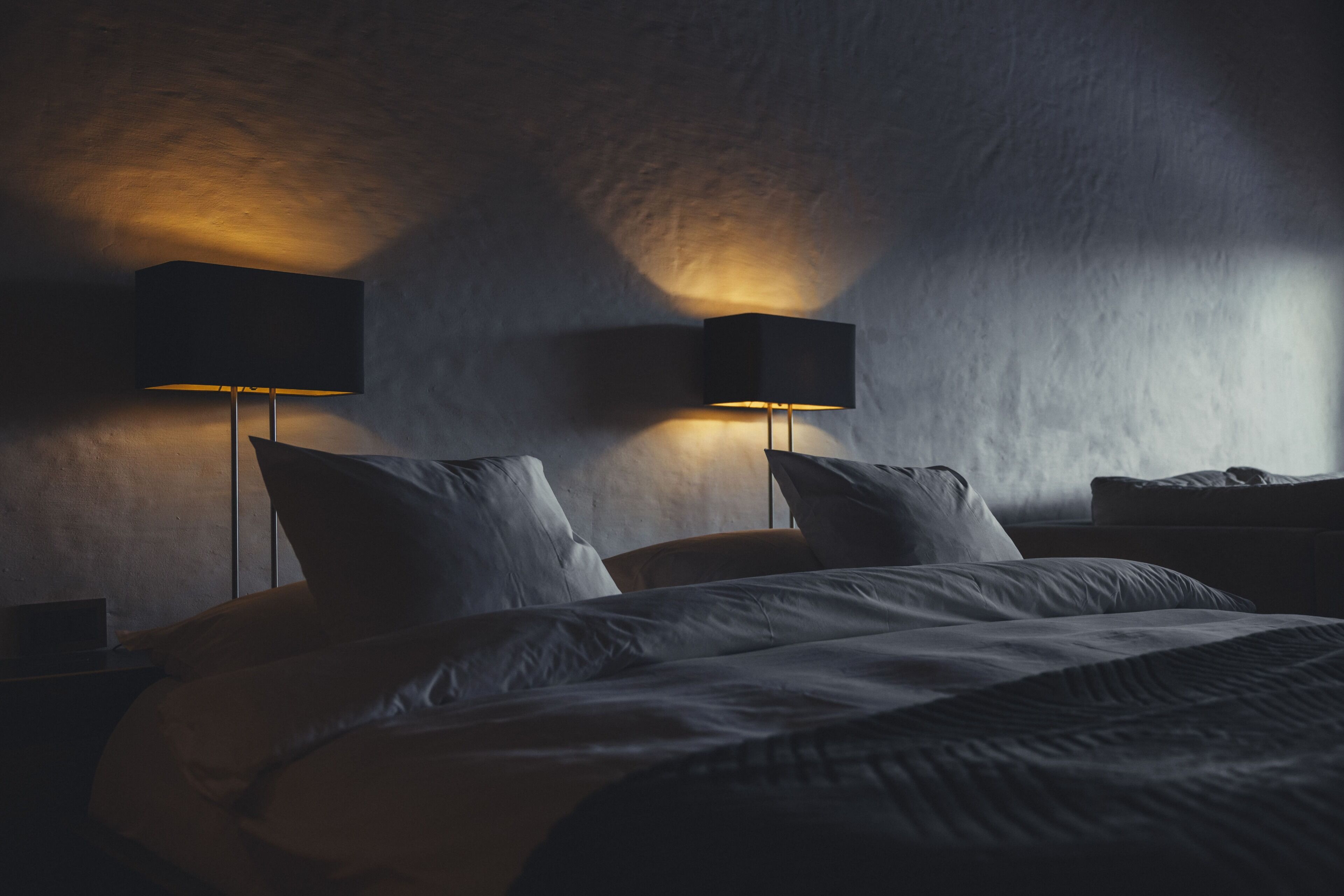 A dimly lit bedroom with a large bed, two bedside lamps, and a nightstand.