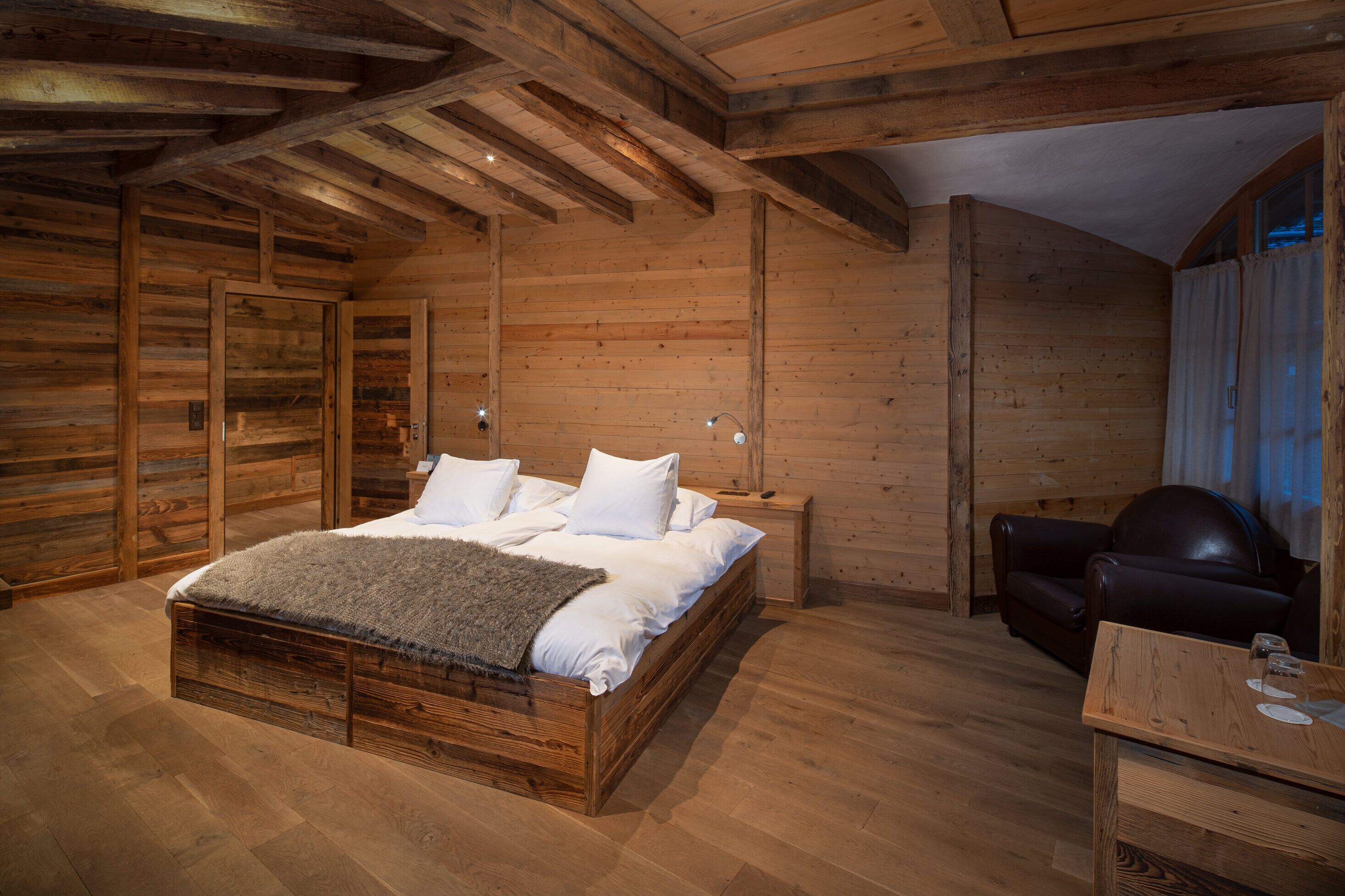 Ein Holzblockhaus-Interieur mit einem Bett, einem Ledersessel und einem kleinen Tisch.