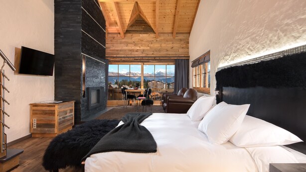 Un dormitorio con una cama grande, chimenea, zona de comedor y vistas a montañas.