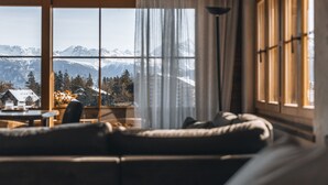 Una sala de estar acogedora con un ventanal que ofrece vistas a montañas nevadas y una cabaña.