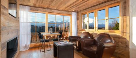 A wooden-paneled room with a fireplace, leather sofa, and a dining area with a table and chairs.