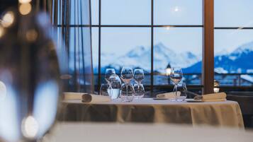 A dining table with multiple wine glasses and a menu, set against a backdrop of a mountain view through large windows.