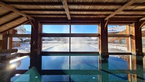 Una piscina interior con vista despejada a un paisaje nevado a través de amplios ventanales.