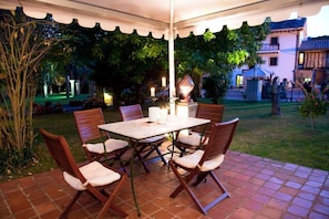 Eine Außenpatio mit Tisch und Stühlen, umgeben von viel Grün und einem Gebäude im Hintergrund.