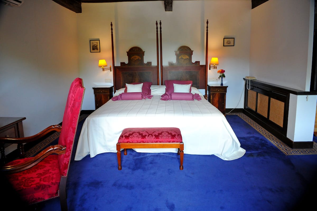 A bedroom with a large bed, a bench, a chair, and a mirror.