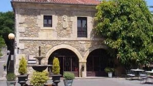 Un bâtiment en pierre avec un toit en tuiles, deux portes cintrées et un grand arbre devant.