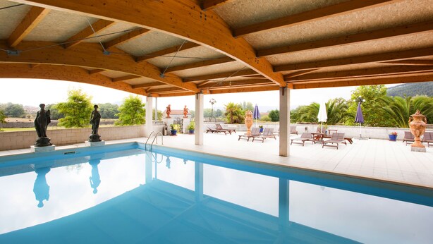 Une piscine surmontée d’une pergola en bois, entourée de chaises longues et de plantes en pot.