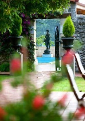 Ein Gartenweg führt zu einer Statue, begleitet von Kübelpflanzen an beiden Seiten.