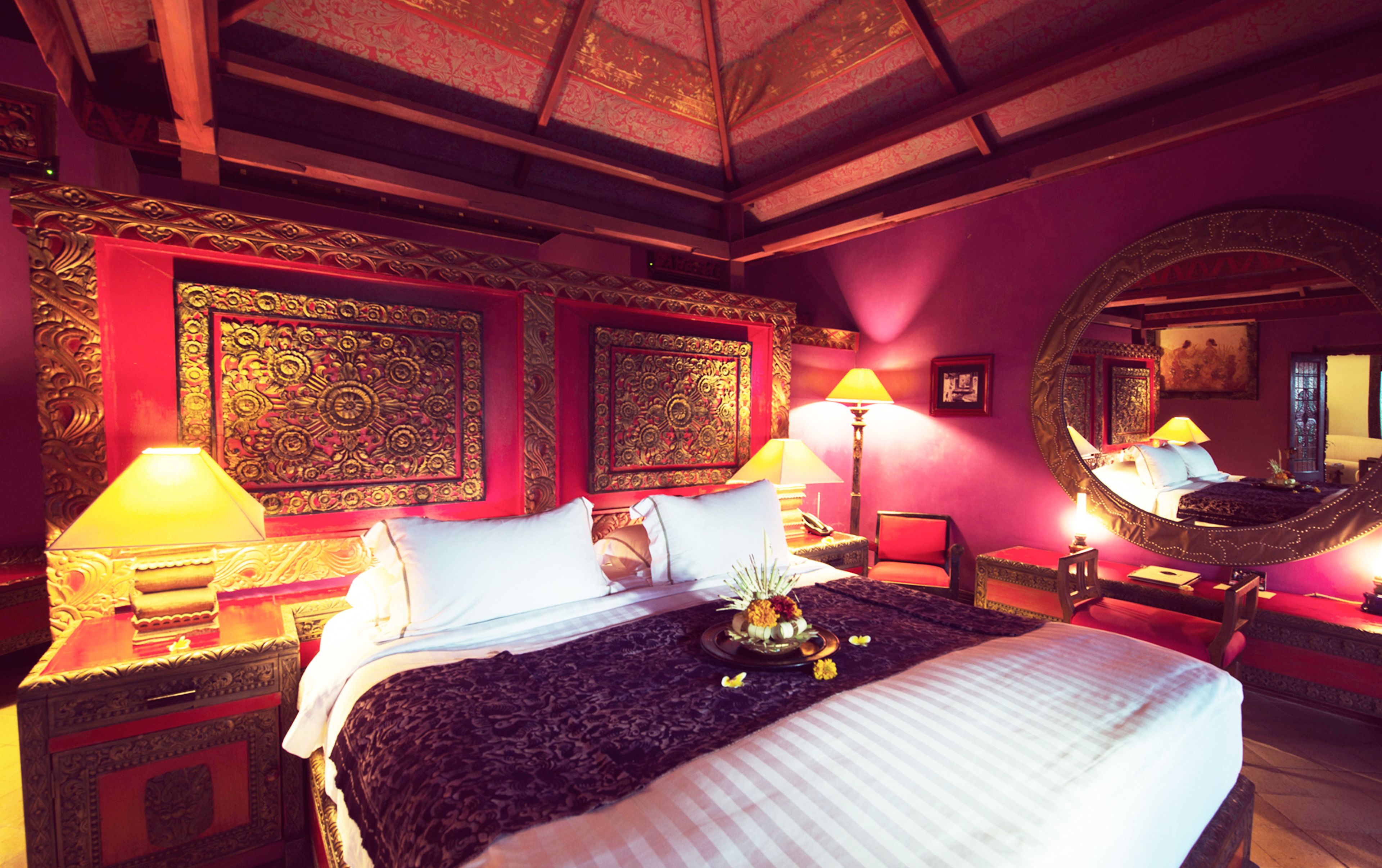 A room with a bed, two lamps, a mirror, and ornate wall decorations.