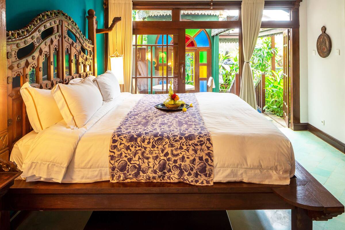 A large bed with a decorative headboard, a floral bedspread, and a small table with a fruit arrangement.