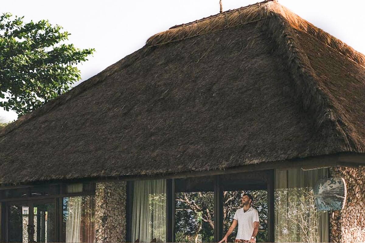 A traditional thatched-roof house with a stone balcony overlooking a lotus pond.