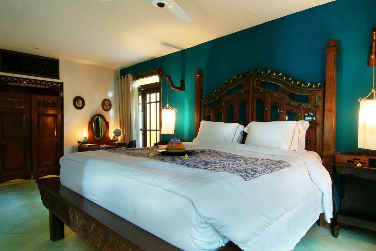A bedroom with a large bed, wooden headboard, and a nightstand with a lamp.