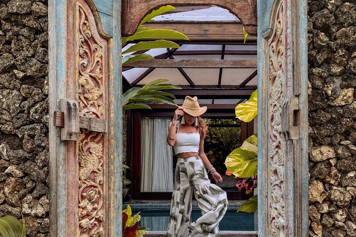 A person standing in a doorway with ornate carvings, a stone wall, and tropical plants.