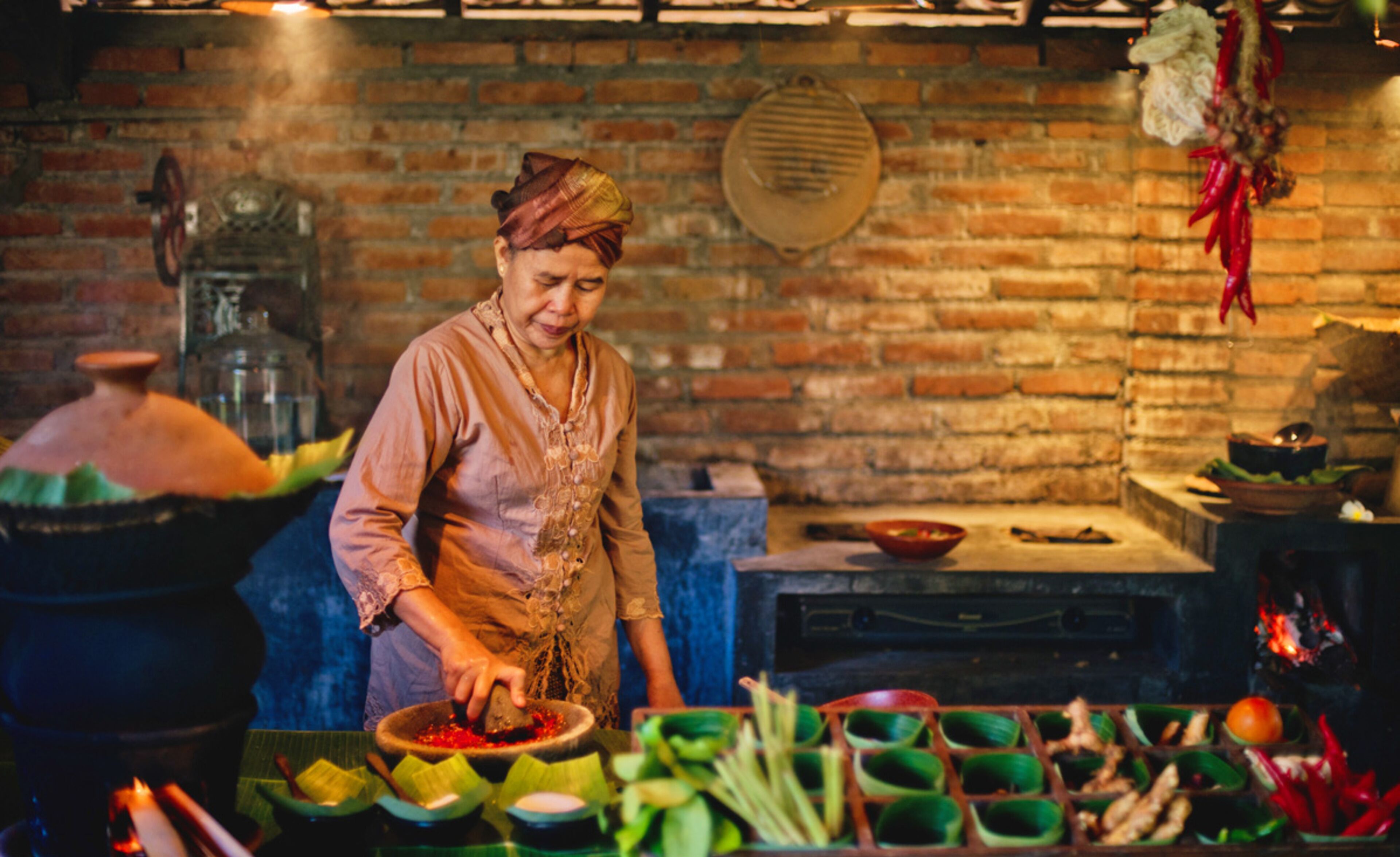 A person preparing food in a kitchen with brick walls, a traditional stove, and various cooking utensils and ingredients.