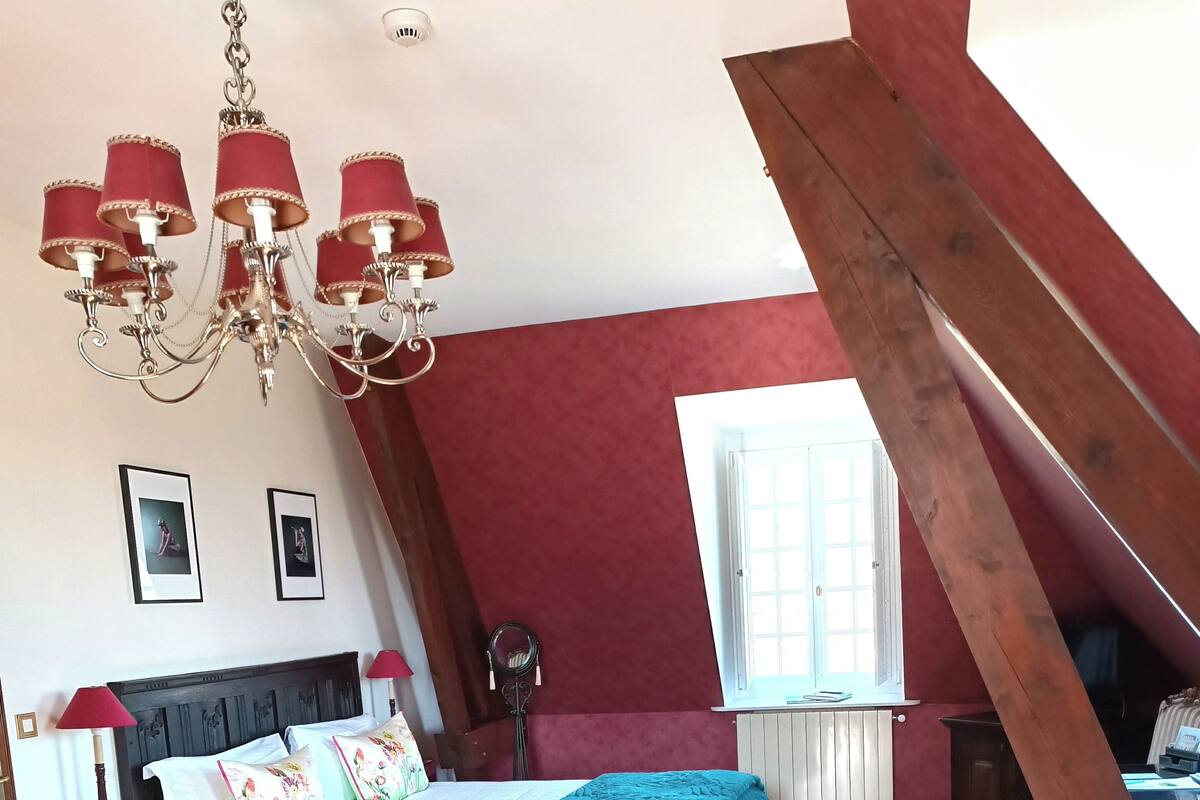 Un dormitorio con techo de madera, una cama con colcha color turquesa, una araña y dos mesitas con manzanas.
