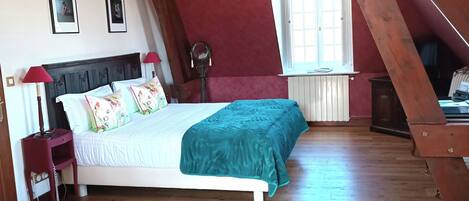 Un dormitorio con techo de madera, una cama con colcha color turquesa, una araña y dos mesitas con manzanas.