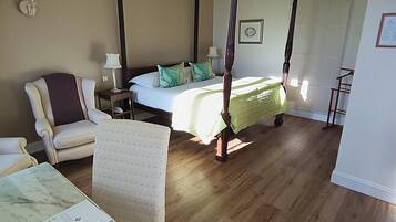 A four-poster bed with a green bedspread, a chair, a bedside table, and a lamp.