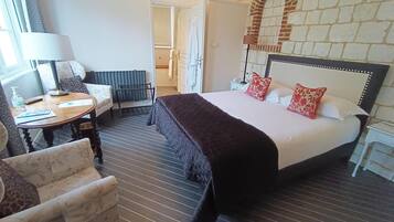 A hotel room with a large bed, a desk with a lamp, a chair, and a radiator.