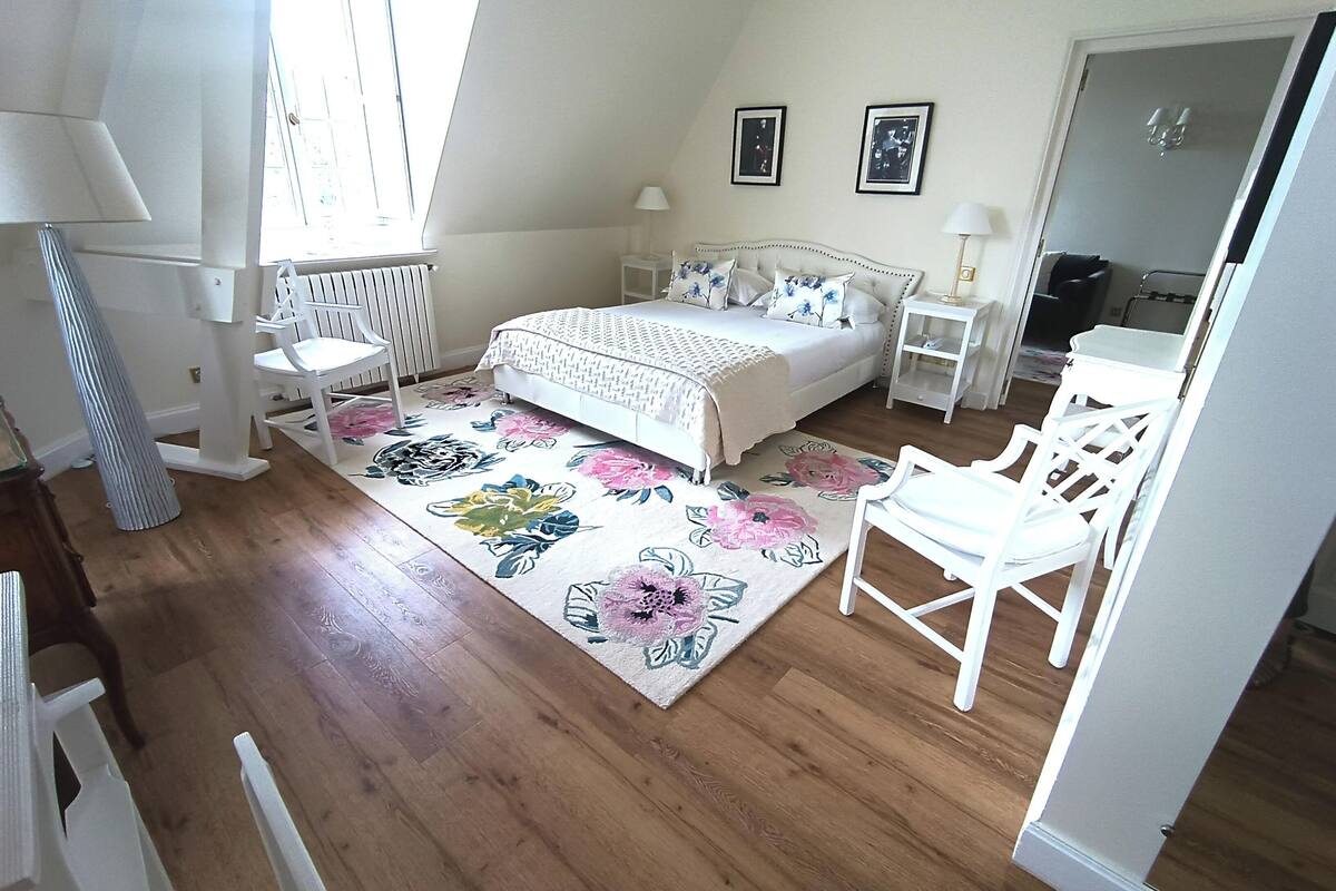 Un dormitorio con una cama, dos mesitas de noche, una silla, un tocador, una ventana y una puerta.