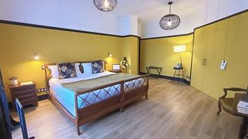 A hotel room with a wooden bed, two bedside tables, a desk, a chair, and a wardrobe.