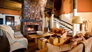 A cozy living room with a stone fireplace, wicker furniture, and a staircase. - The Motse - Tswalu Kalahari Luxury Private Game Reserve (Kuruman)
