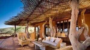 An outdoor lounge area with wicker furniture, a wooden deck, and a thatched roof structure. - The Motse - Tswalu Kalahari Luxury Private Game Reserve (Kuruman)