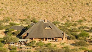 A thatched-roof building with multiple rooms, surrounded by sparse vegetation. - The Motse - Tswalu Kalahari Luxury Private Game Reserve (Kuruman)