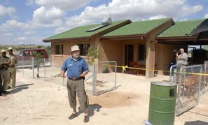 A building with a green roof, a fenced area, and a person standing in front. - The Motse - Tswalu Kalahari Luxury Private Game Reserve (Kuruman)