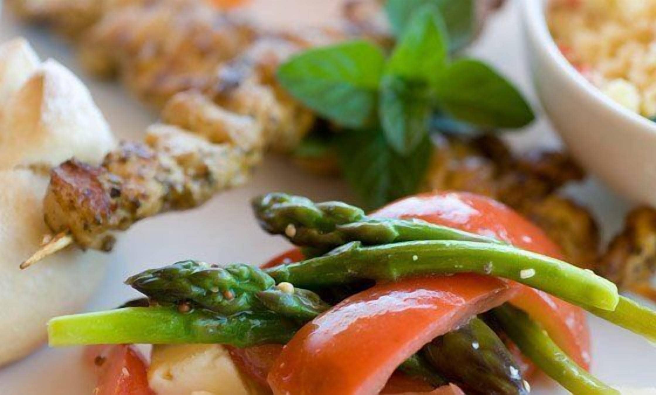 A plate with grilled chicken, asparagus, and tomatoes.