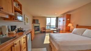 A hotel room with a bed, a desk, a chair, a fireplace, and a view of the outdoors. - Inn at Big White (Beaverdell)