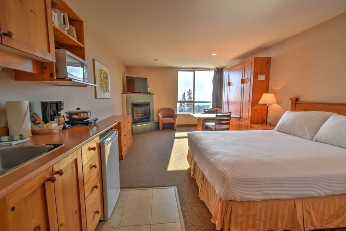 A hotel room with a bed, a desk, a chair, a fireplace, and a view of the outdoors.