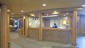 A reception area with a wooden reception desk, a clock, and a wall-mounted menu board. - Inn at Big White (Beaverdell)