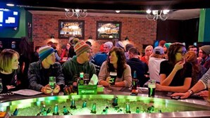 A bar with a brick wall and framed pictures. There are people seated at the bar, and bottles are visible on the counter. - Inn at Big White (Beaverdell)