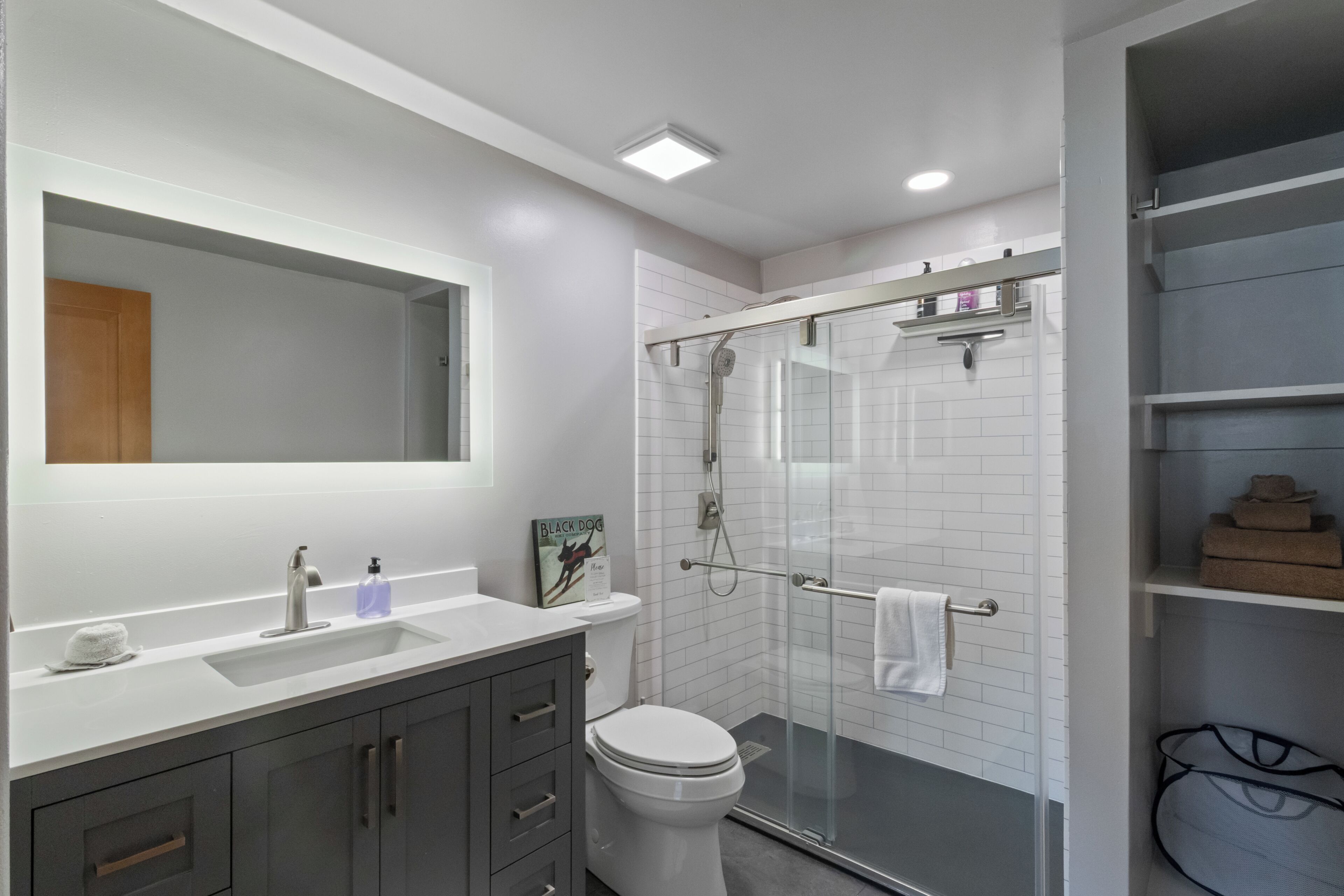 Un baño moderno con cabina de ducha de vidrio, un lavabo blanco y un espejo grande.