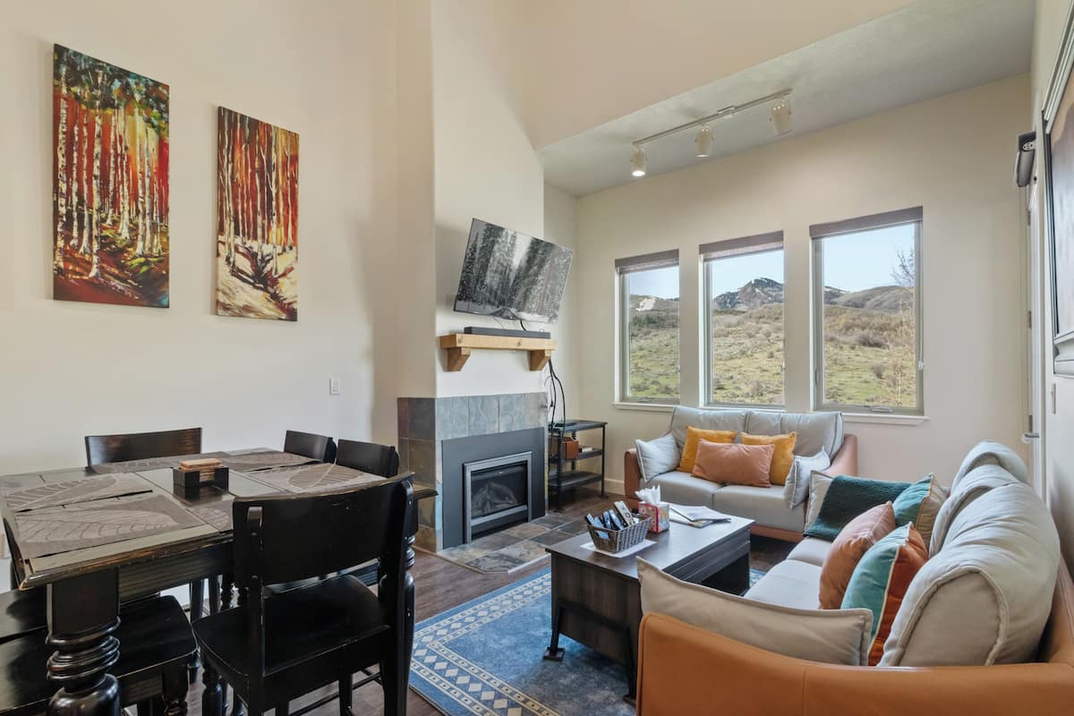 A spacious living area with a fireplace, a dining table, and a sofa with colorful cushions.