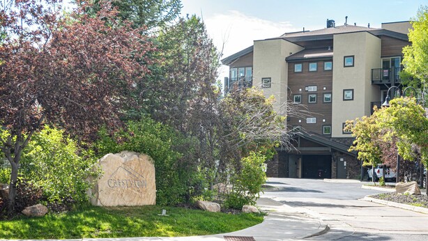 A stone sign with "Crestview" written on it, surrounded by greenery and a building with multiple windows and balconies. - Crestview Condominiums by All Seasons Resort Lodging (Park City)