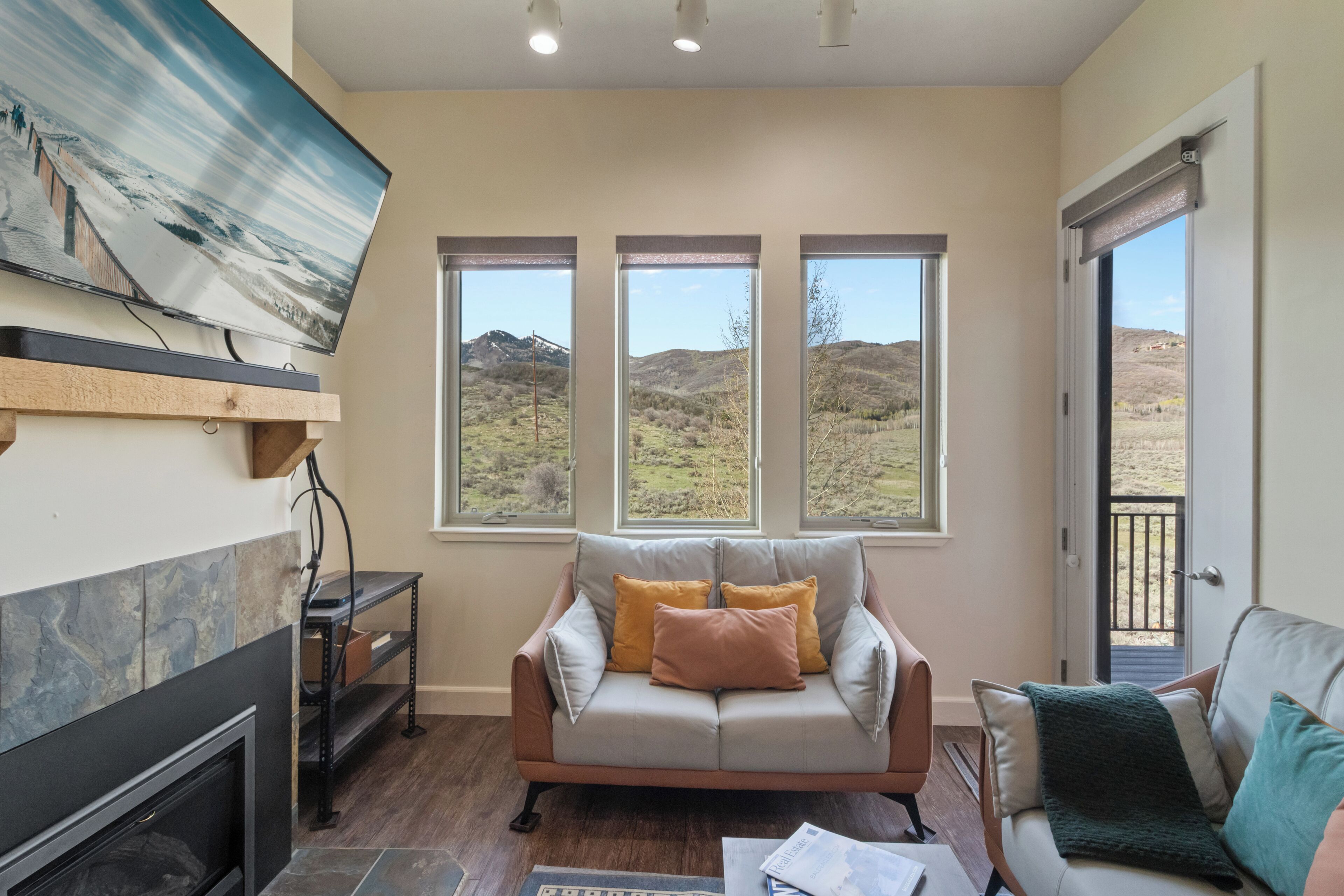 A living room with a fireplace, a sofa, a television, and a view of a mountainous landscape through large windows.