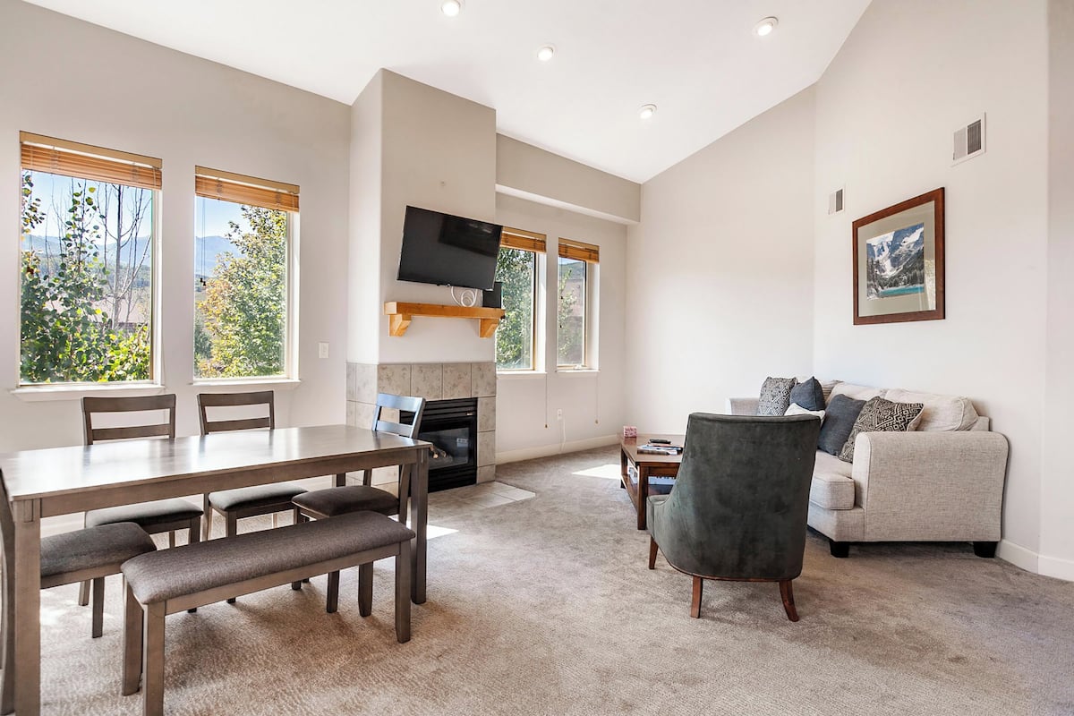 A spacious living room with a fireplace, a dining area with a table and benches, a gray armchair, and a sofa.