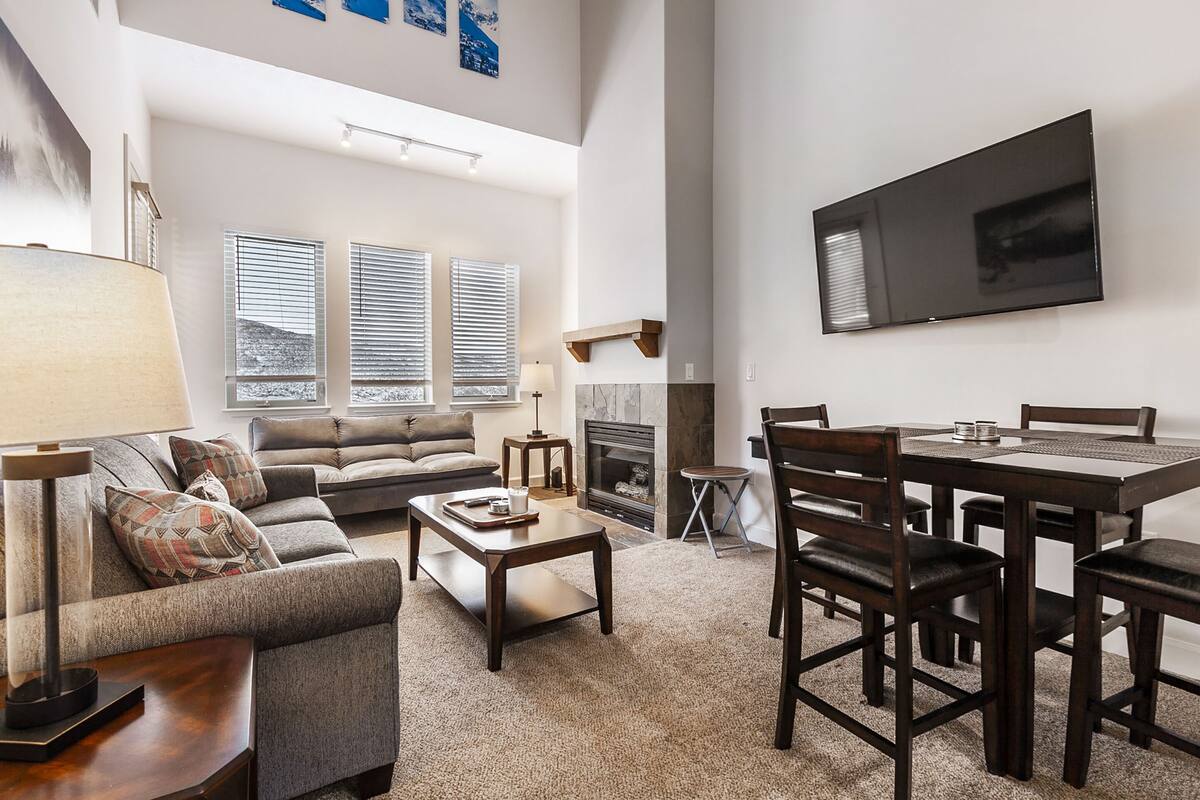 A spacious living room with a fireplace, a dining area, and a large TV mounted on the wall.