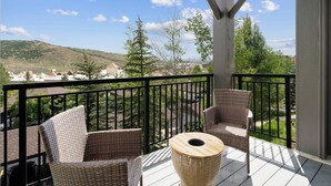A balcony with wicker chairs and a table, overlooking a residential area and hills. - Crestview Condominiums by All Seasons Resort Lodging (Park City)